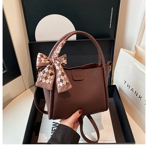 Detail view of brown pebbled leather bucket bag with fashion logo and silk scarf knot