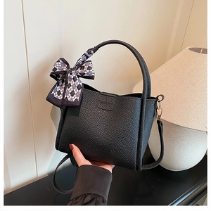 Close-up of black lychee texture bucket bag with a checkered bow tie and detachable strap
