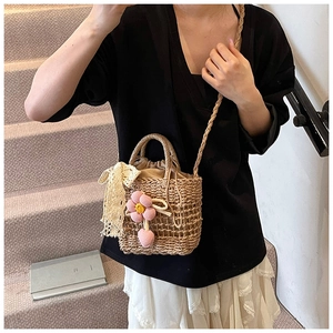 Detail of straw woven bucket bag with floral charms and white lace bow decoration