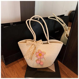 Detail of a handmade cream woven tote bag featuring a lace bow and pink crochet flower charm