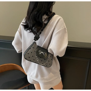 Detail of grey polka dot underarm bag with black leather flap and silver bow buckle
