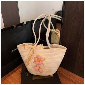 Close-up of a cream woven straw tote bag with lace bow and crochet pink flower charm