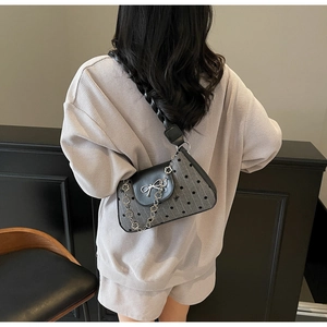 Close-up of grey polka dot baguette bag with black leather flap and silver bow detail
