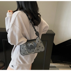 Detail of grey bow-patterned shoulder bag with black flap and silver bow buckle on a model