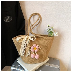 Detail of straw woven tote bag featuring white lace bows and pink crochet flower charms