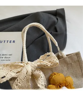 Dettaglio della borsa in tessuto beige con fiocco di pizzo, ciondolo a fiore e manici