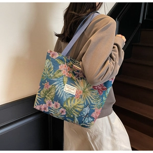 Detail of floral canvas tote bag showing tropical leaves print and woven shoulder strap