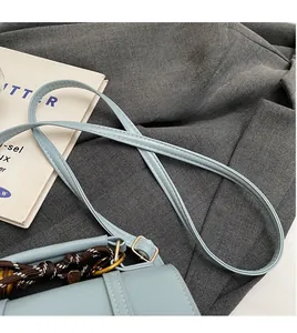 Detail of light blue crossbody bag with braided rope strap on grey suit fabric