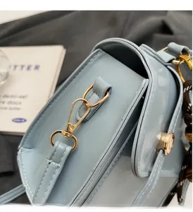 Detailed shot of glossy light blue crossbody bag featuring premium gold metal hardware