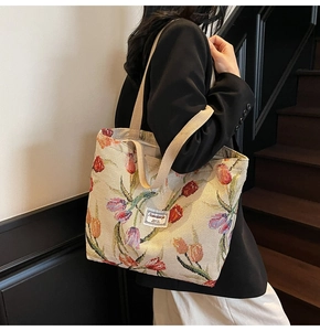 Close-up of cream knit tote bag featuring colorful tulip embroidery and textured strap