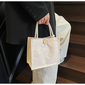 Dettaglio della borsa tote in tessuto trapuntato panna con bottone giallo e manici