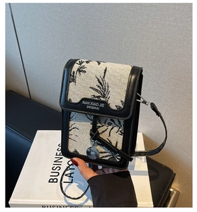 Detailed view of black floral jacquard phone bag with premium leather trim and metal charm