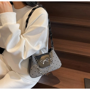 Detail of grey crossbody bag with black heart patterns and silver bow on white hoodie