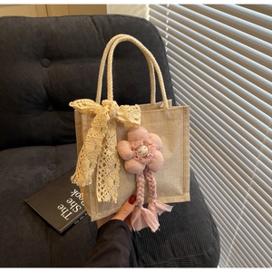 Dettaglio della borsa in juta beige con fiocco in pizzo e ciondolo a fiore di peluche