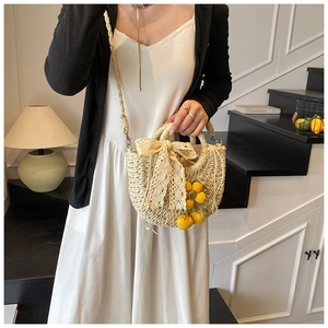 Détail du sac en paille tressé main avec nœud en dentelle et breloques de fleurs tricotées