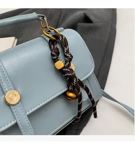 Detail of light blue leather handbag with woven rope charm and golden hardware