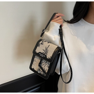 Detail of a vintage floral canvas crossbody bag with black leather trim and silver charm