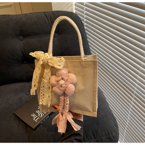 Dettaglio della borsa in juta intrecciata con fiocco in pizzo e ciondolo a fiore rosa