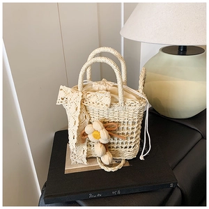 Detail of cream handmade straw bag featuring lace bows, woven floral charms and drawstring