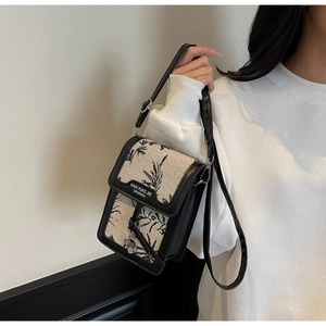 Detail of canvas bag with black floral print and leather strap worn by a model
