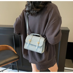 Detail view of a light blue square crossbody bag with gold metallic buckles on a model