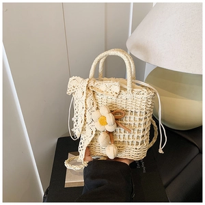 Detail of hand-woven beige straw handbag with lace bow, floral charm and drawstring lining