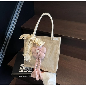 Dettaglio della borsa tote in tessuto beige con fiocco di pizzo e ciondolo a fiore rosa