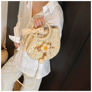 Détail du sac en paille avec nœud en dentelle, fleur au crochet et pompon
