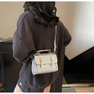 Silver mirror-finish satchel with gold rivet details worn over a charcoal hoodie