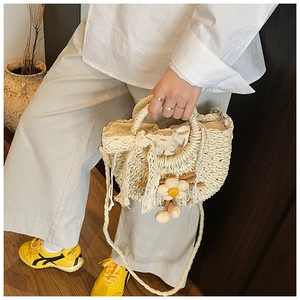 Détail du sac seau en paille tissé main avec nœud en dentelle et pendentif fleur