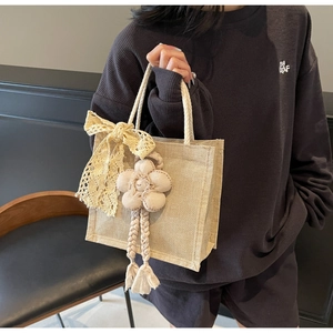 Dettaglio della borsa in juta con fiocco in pizzo crema e ciondolo floreale con nappa