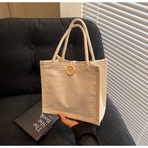 Dettaglio della borsa in tela trapuntata beige con bottone in legno e manico in corda