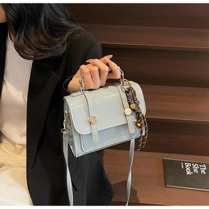 Close-up of light blue leather handbag with gold metal accents and brown woven charm