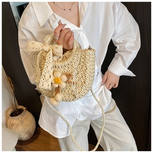 Détail du sac en paille tissé beige avec nœud en dentelle et breloque fleur au crochet