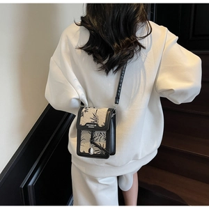 Detail of a white canvas crossbody bag with black plant pattern and leather trim on a model