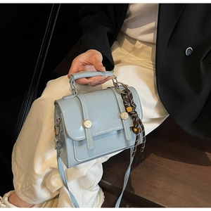 Close-up of light blue flap square bag with woven rope charm on textured faux leather