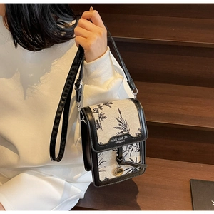 Detail of canvas crossbody bag with black floral print and leather logo tag on a model