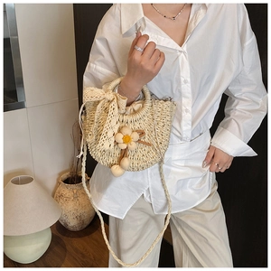 Détail du sac seau en paille crème avec nœud en dentelle, breloque fleurie et bandoulière