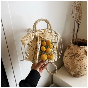 Detail of straw woven bucket bag with beige lace bow, crochet flower and shoulder strap