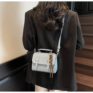 Detail of light blue crossbody bag with gold buttons and silk scarf on wooden stairs