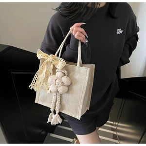 Dettaglio borsa tessuta beige con fiocco in pizzo e ciondolo a fiore sulla scala