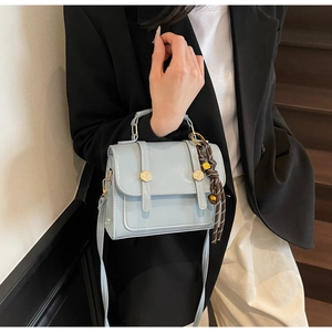 Detail view of light blue crossbody bag featuring gold buttons and woven rope accent