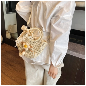 Détail du sac seau en paille tissée avec nœud en dentelle et breloque florale