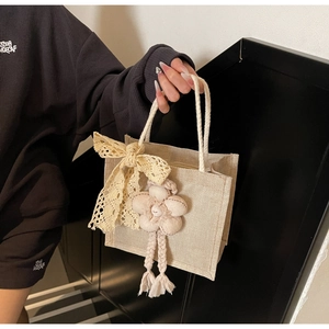 Dettaglio di borsa tessuta bianco sporco con fiocco di pizzo e ciondolo a fiore