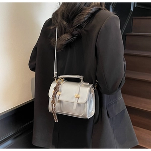Detail of silver metallic crossbody bag with gold buckles and woven charm on black blazer