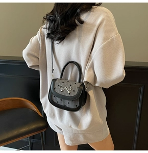 Detail of grey polka dot crossbody bag with silver bow accent worn with casual outfit