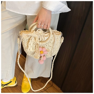 Détail du sac en paille avec nœud en dentelle et breloque fleurie pour l'été
