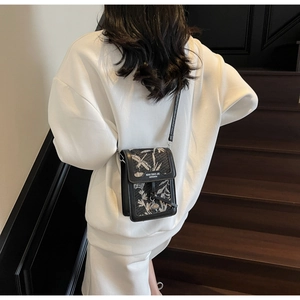 Close-up of black crossbody bag with white leaf embroidery and metal charm detail
