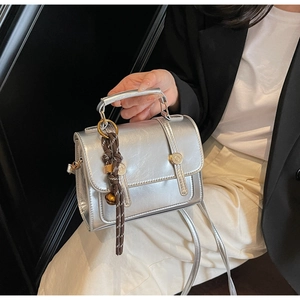 Detail of silver mirror finish PU leather crossbody bag with brown woven tassel charm