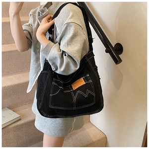 Detail of black denim tote bag showing white contrast stitching and brown logo patch